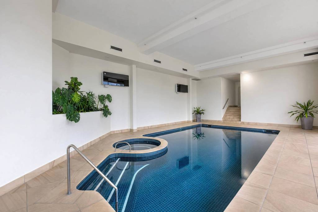 Large heated indoor pool with spa, seating and gardens visible through windows