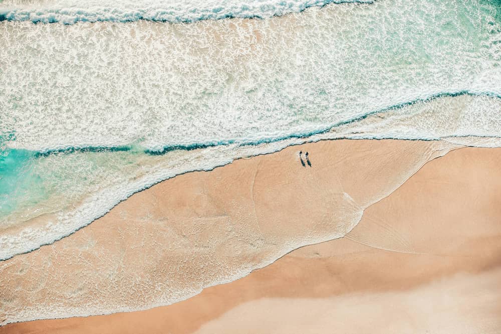 Two people walking along the shoreline from above