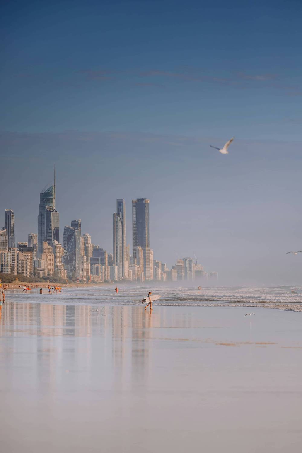 A surfer at sunset against the Gold Coast skyline reflected on wet sand