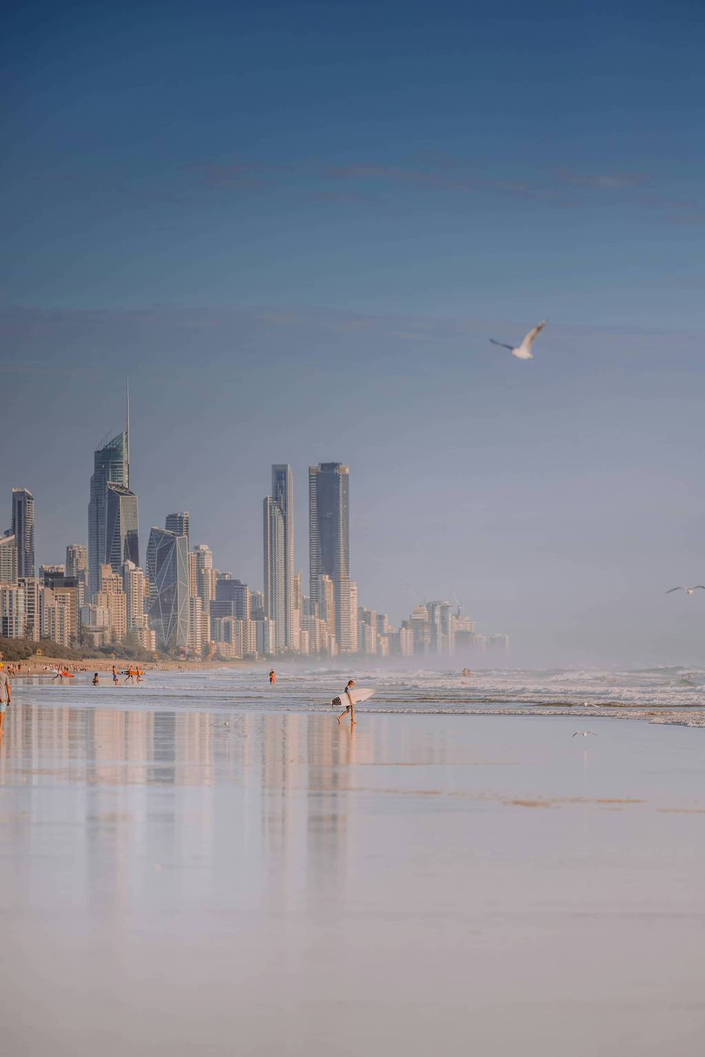 A surfer at sunset against the Gold Coast skyline reflected on wet sand