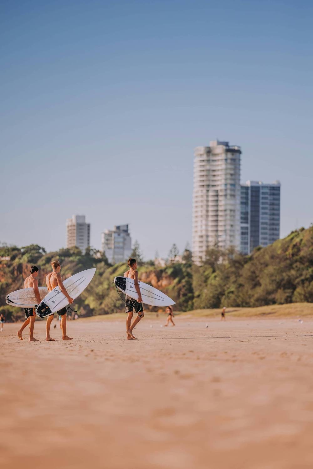 Surfers walking on Main Beach with apartment towers behind