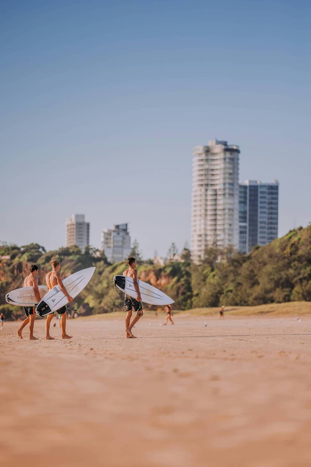 Surfers walking on Main Beach with apartment towers behind