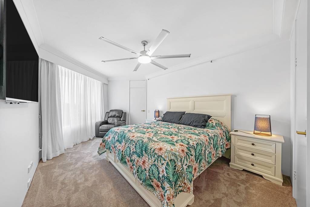 Bedroom with floral bedcover, ceiling fan, television and armchair