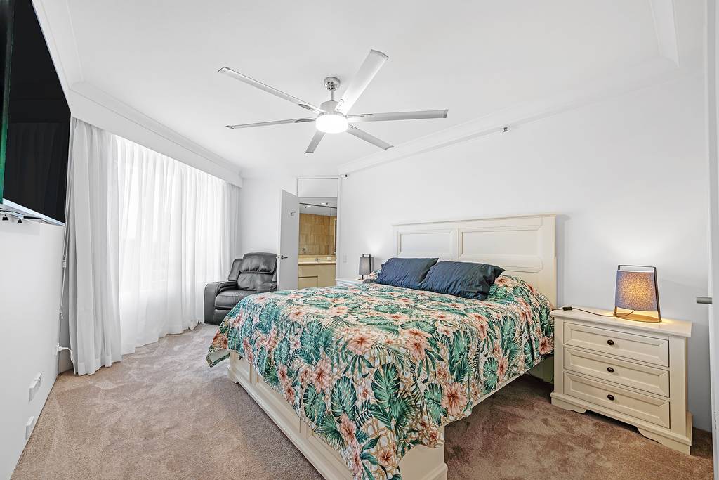 Bedroom with floral bedcover, ceiling fan and upholstered armchair