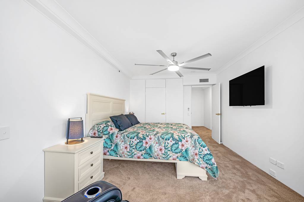 Bedroom with floral bedcover, ceiling fan, television and bedside lamps