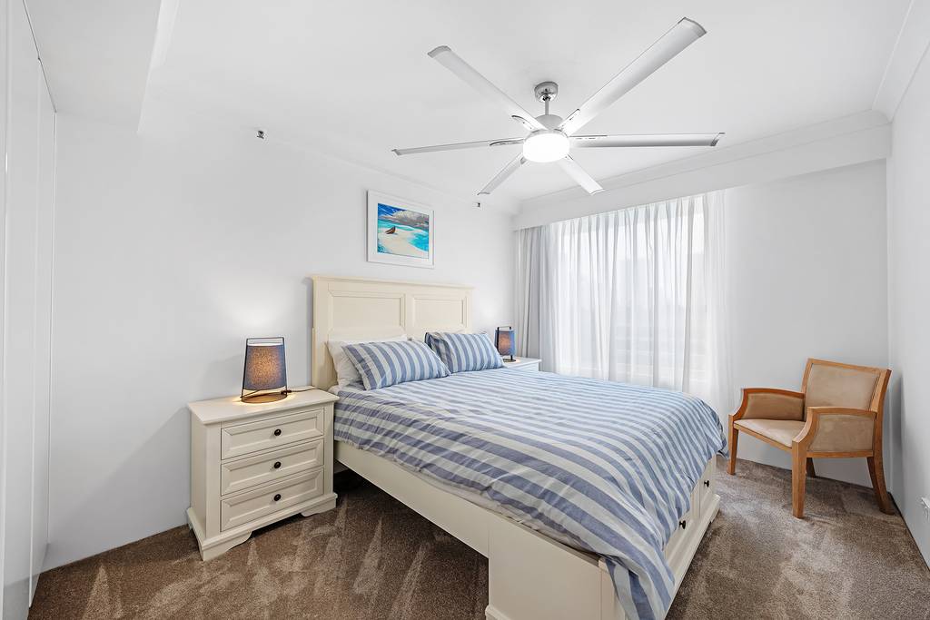 Bedroom with striped bedding, ceiling fan, bedside lamps and armchairs