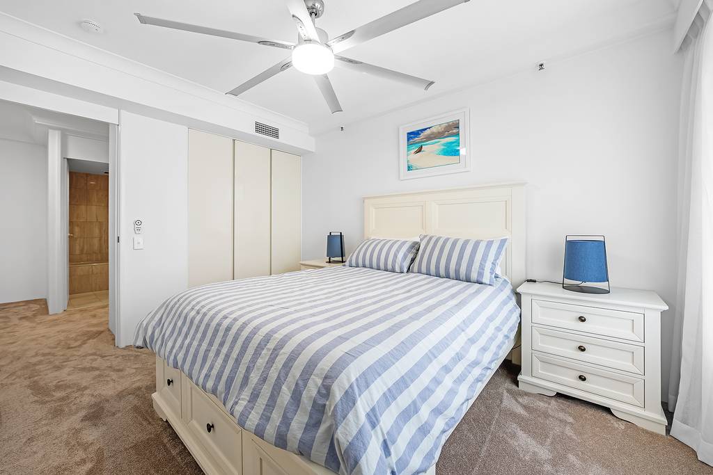Bedroom with striped bedding, ceiling fan, wardrobe and bedside tables