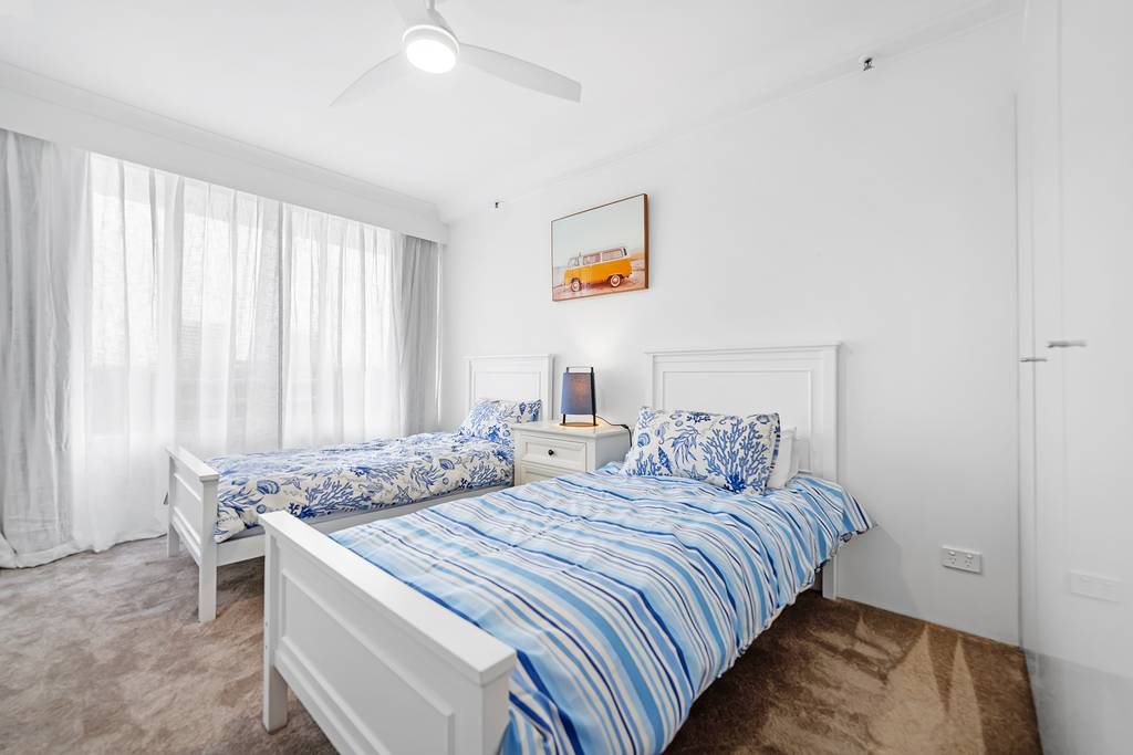 Twin bedroom with blue striped bedding, ceiling fan and curtains