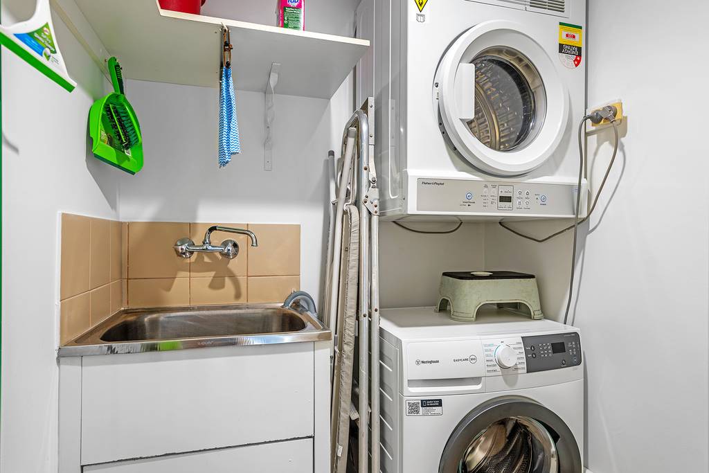 Laundry with stacked washer and dryer, utility sink and ironing board