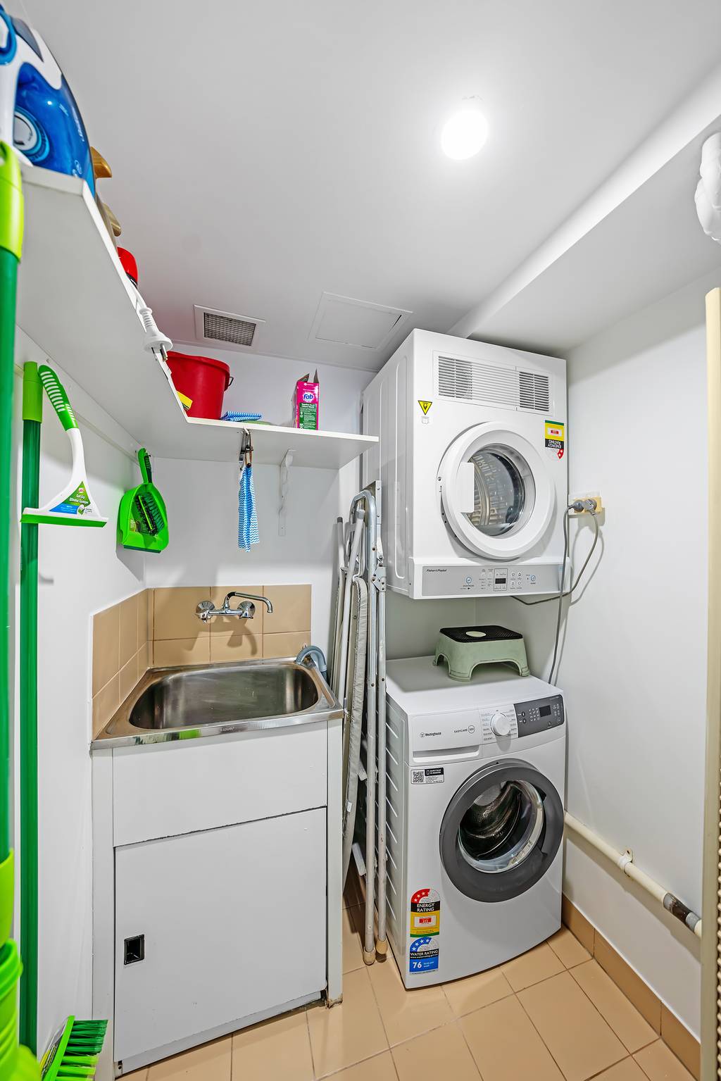 Laundry with stacked washer and dryer, utility sink and cleaning supplies
